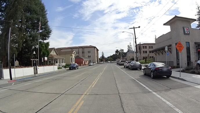 A solid white line separates the traffic lane from the parking lane. A regulatory sign says 24 Minute Parking, 9 AM to 5 PM, Monday through Friday. A warning sign says to share the road with cyclists. (© 2016 Bryan Housel, CC BY-SA 4.0.)