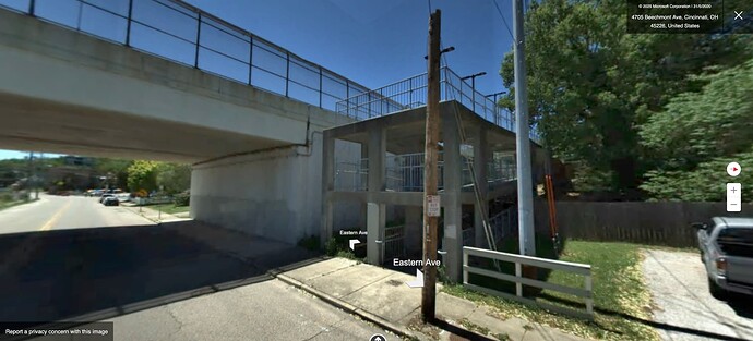 A concrete frame structure supporting a spiral pedestrian ramp connects Eastern Avenue to a highway overpass.