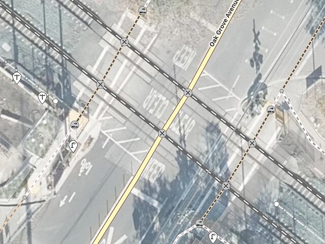 Oak Grove Avenue crosses two railroad tracks. The sidewalks on either side also cross both tracks. The crossings are marked with standard transverse lines.