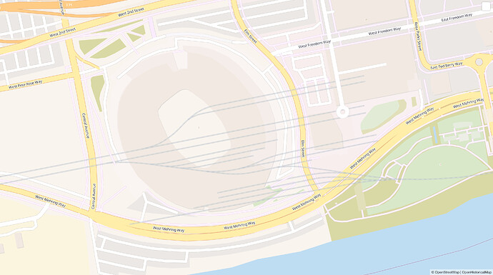A football stadium, parking lots, and a riverfront park with faint, blurred-out railroad tracks superimposed. The tracks extend from the west and branch out numerous times on land now occupied by the stadium. Some of the tracks then merge into another line that extends to the east, on what is now a park.
