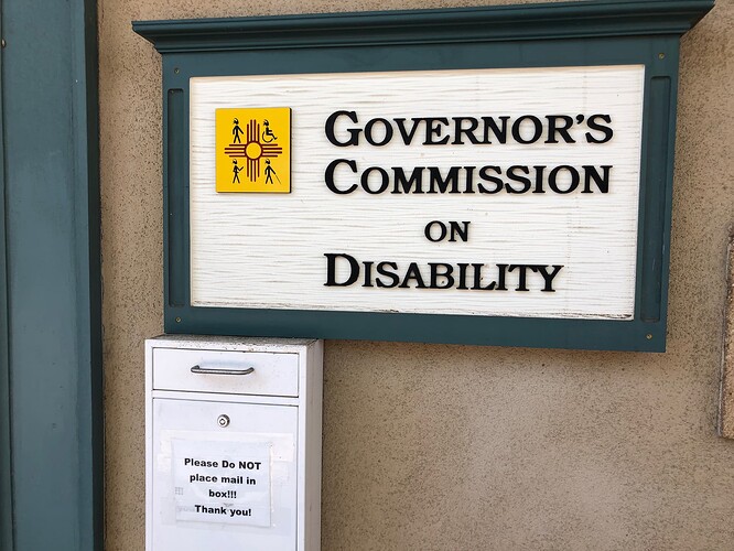 A white box on a wall, under the sign for the Governor’s Commission on Disability, has a door with a handle and a sign saying: Please Do NOT place mail in box!!! Thank you!