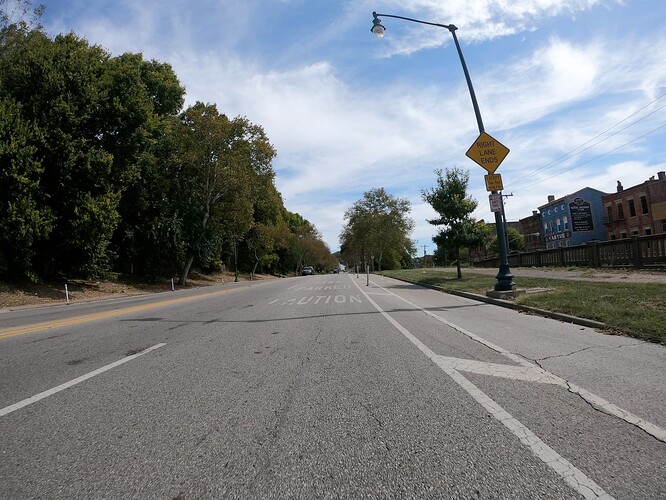 A marking on the right lane says Caution Parked Cars. A warning sign says Right Lane Ends Except 7 AM to 9 AM Monday to Friday. Below it, a regulatory sign says No Stopping No Parking Any Time, but further down there are signs allowing parking between 7 AM and 9 PM weekdays. (© 2019 realadamp, CC BY-SA 4.0.)