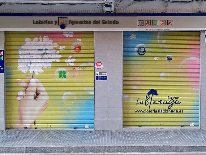 Mural en la persiana de cierre de una administración de lotería representando una mano sosteniendo una flor de biznaga y unas burbujas de jabón conteniendo elementos que hacen referencia a la lotería y a la suerte con un fondo multicolor de color amarillo, celeste y rosa.