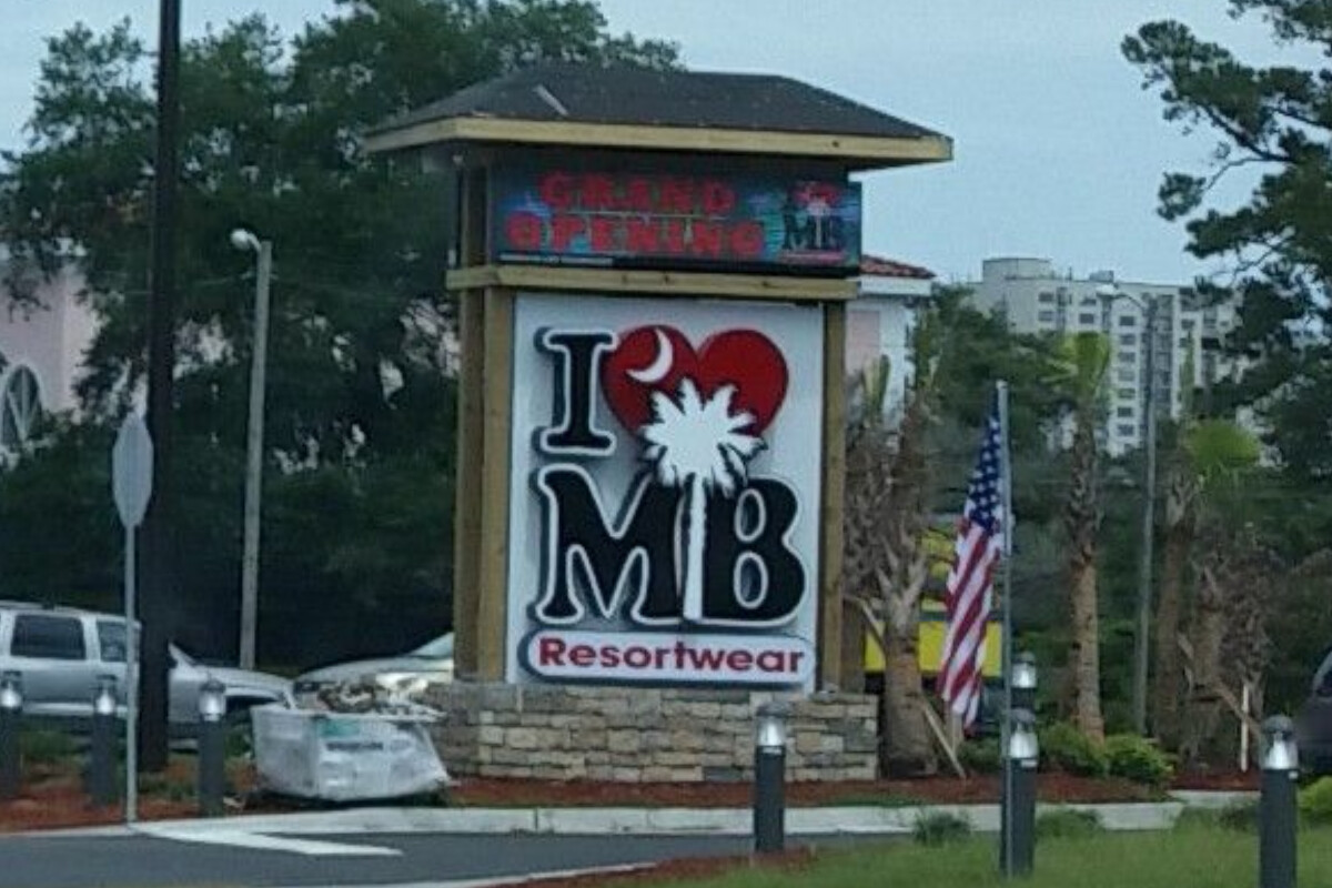 Sign for a shop whose logo consists of the letters I, B, and M in black monospaced type, with a white crescent moon inscribed on a red heart after the I and a white palmetto tree between the M and B (© 2016 Duane Gearhart, CC BY-SA 4.0)
