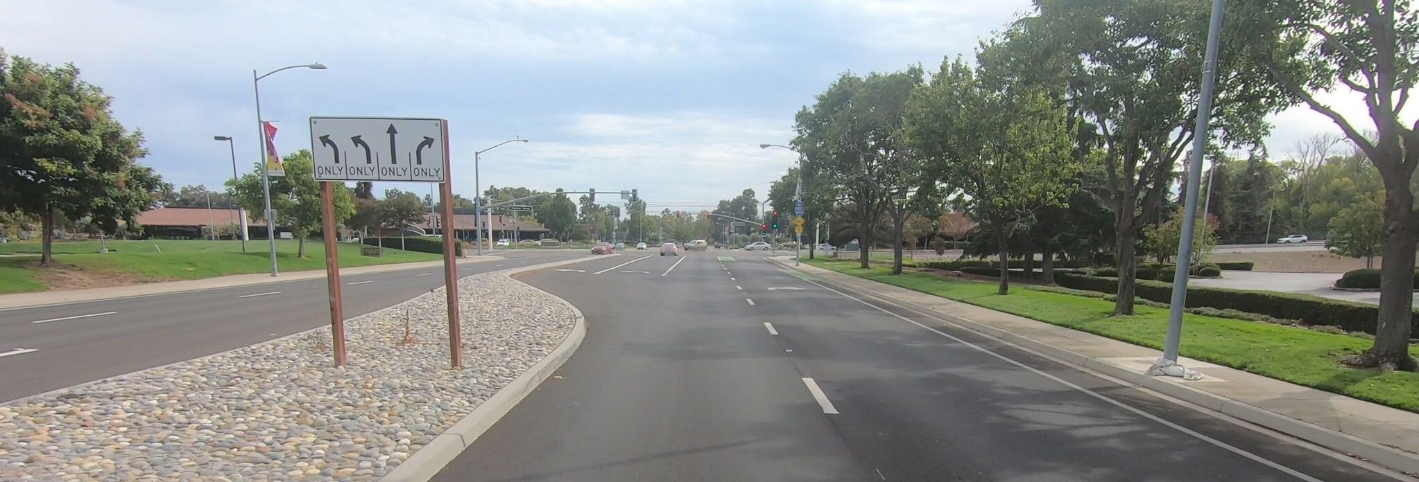 Approaching an intersection, a lane use diagram sign indicates two left turn lanes, a through lane, and a right turn lane, but omits the short through bike lane, marked in green in the distance. (© 2021 networklanman, CC BY-SA 4.0)