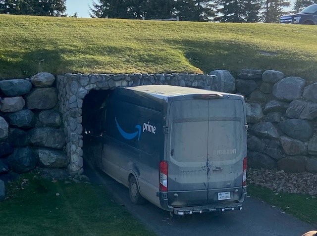 A delivery van in Amazon Prime livery on a narrow, paved path, wedged into a box culvert with a vertical clearance inches shy of the van’s roof. The roof appears to be dented slightly, suggesting a collision with the tunnel’s stone ceiling reinforcement. (© 2020 Advance Local Media LLC, fair use for critical commentary about an historic event.)